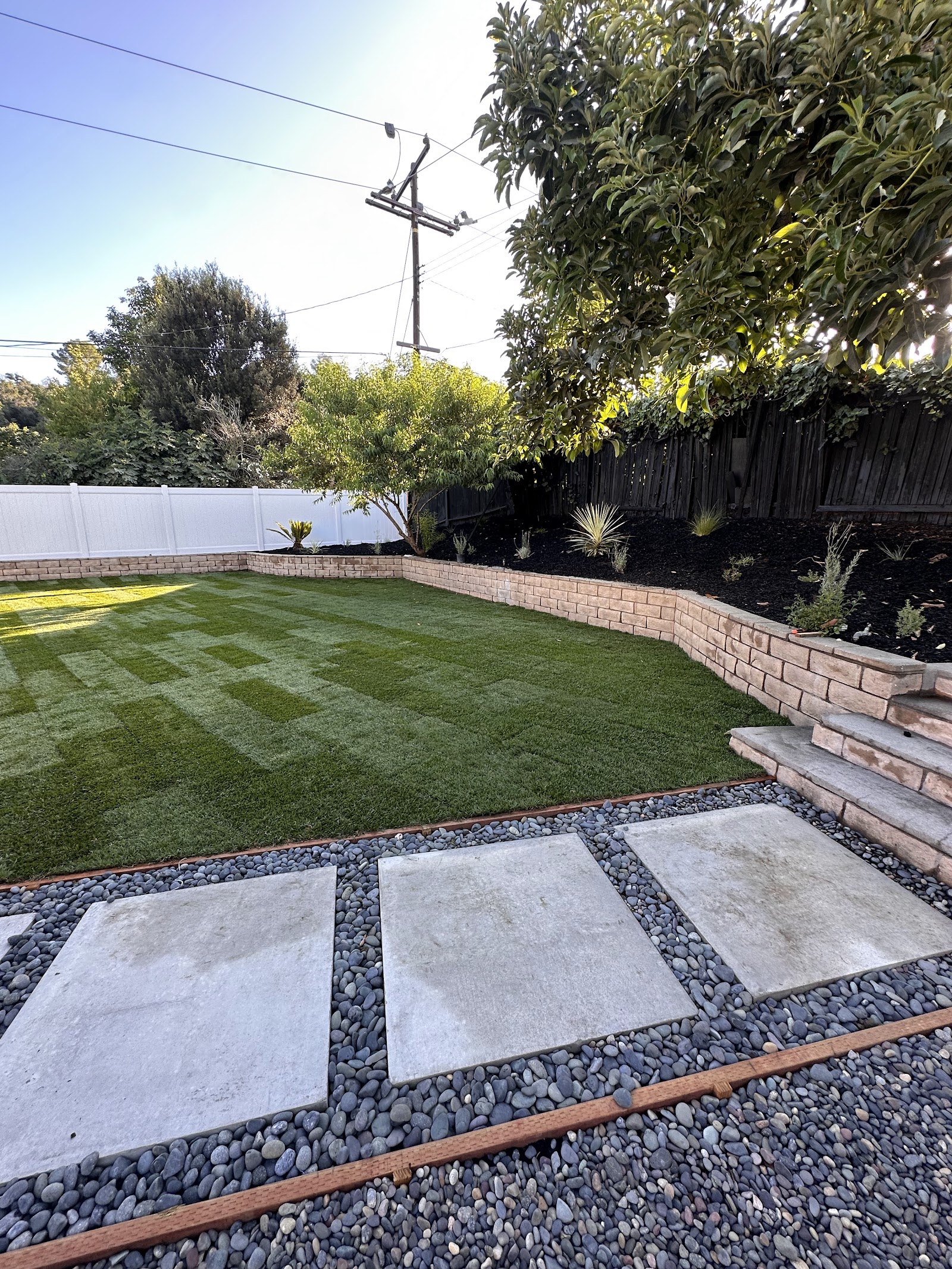 A finished green lawn with large rectangular stepping stones and a decorative gravel border