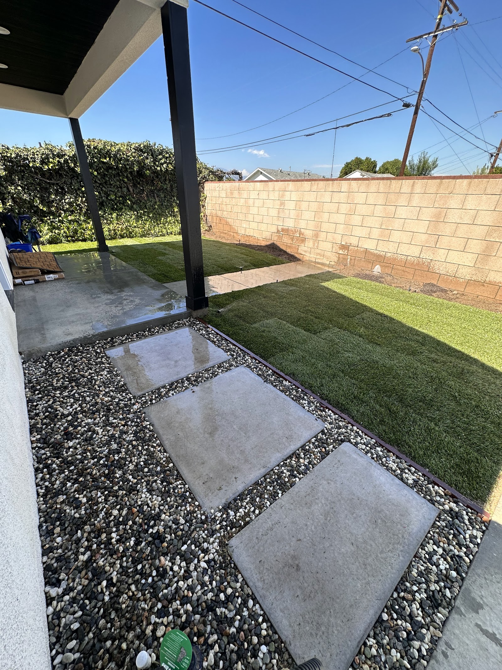Concrete stepping stones with gray pebble borders beside a newly installed lawn and covered patio